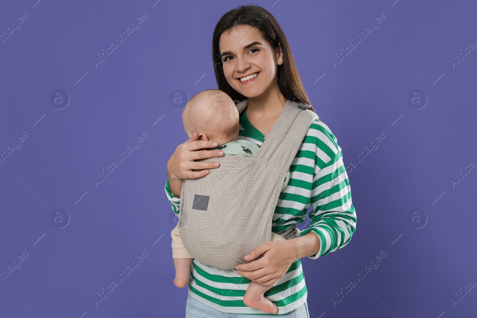 Photo of Mother holding her child in sling (baby carrier) on purple background