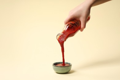 Photo of Woman pouring tasty ketchup from bottle into bowl on beige background, closeup. Space for text