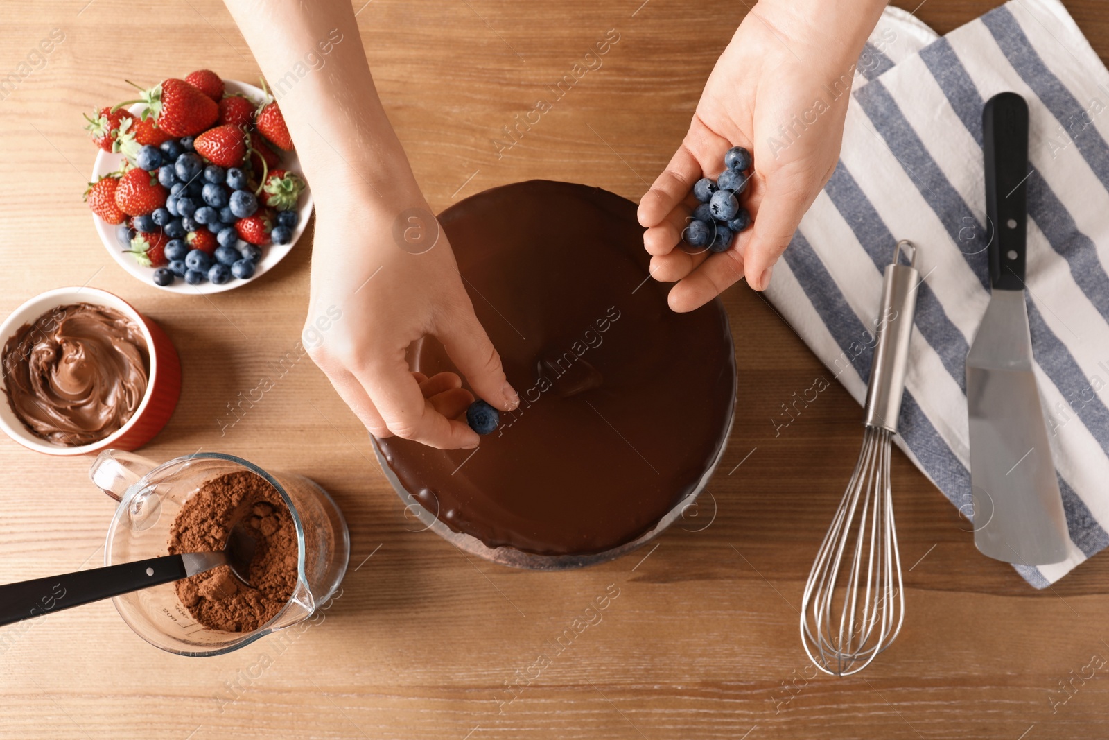 Photo of Baker decorating fresh delicious homemade chocolate cake with berries on table, closeup