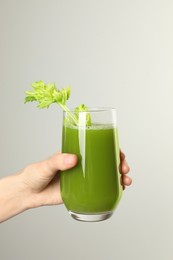Photo of Woman holding glass of delicious celery juice on light grey background, closeup. Space for text