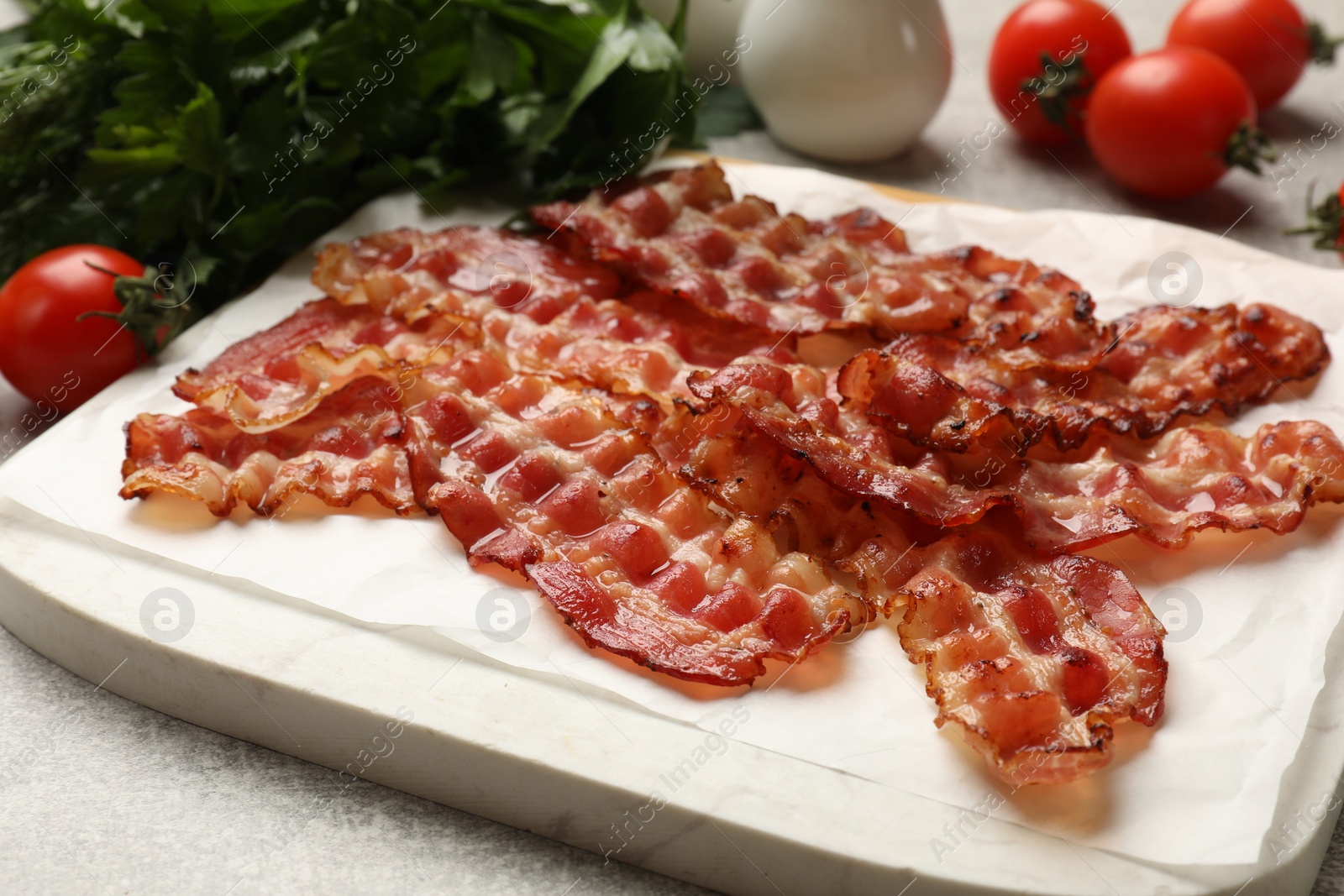 Photo of Fried bacon slices, tomato and parsley on grey textured table, closeup