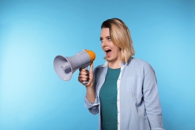 Photo of Portrait of emotional woman using megaphone on color background