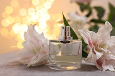 Bottle of perfume and beautiful lily flowers on table against beige background with blurred lights, closeup