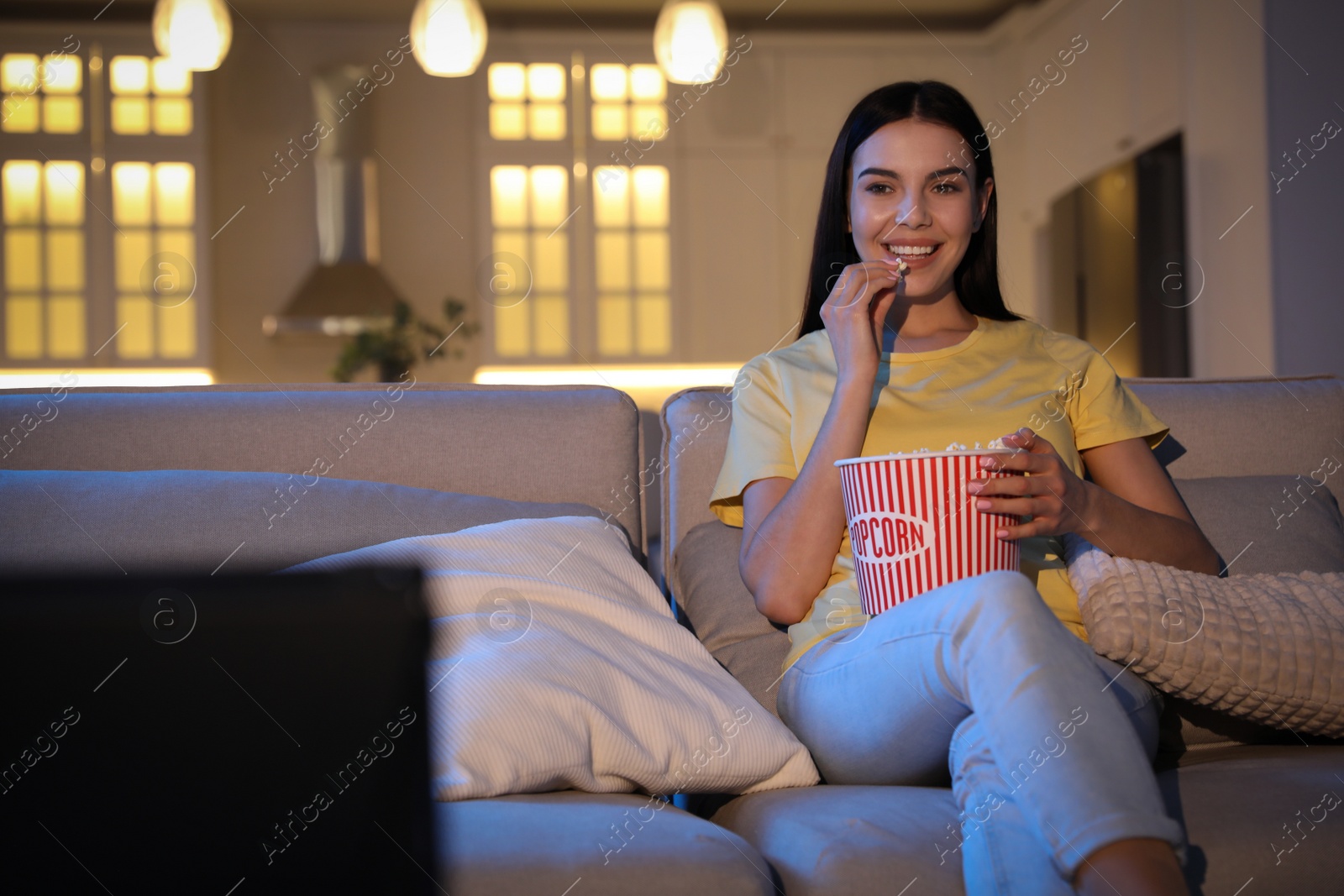 Photo of Young woman watching movie with popcorn on sofa at night, space for text