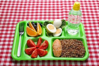 Serving tray with healthy food on checkered background. School lunch
