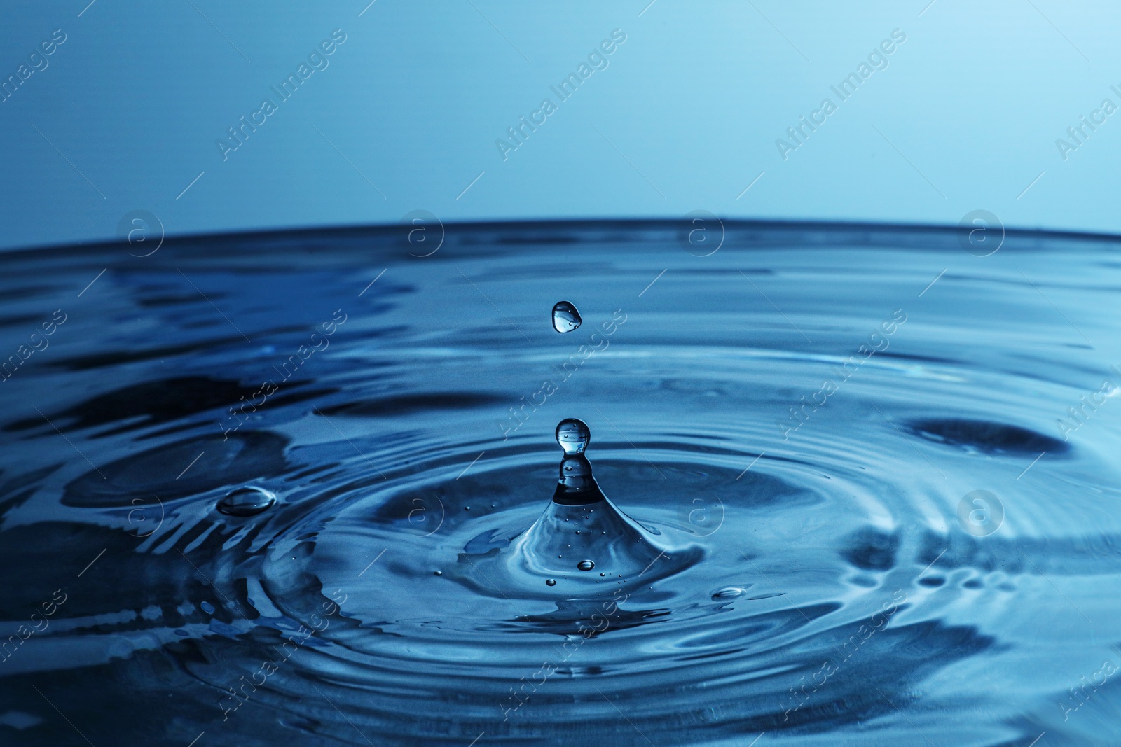 Photo of Splash of clear water with drop on blue background, closeup