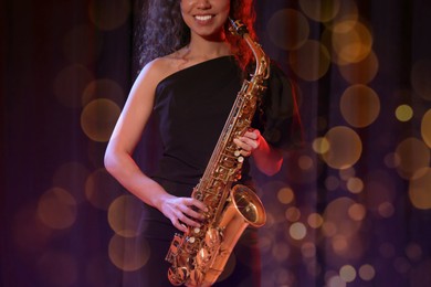 Image of African American woman with saxophone on dark background. Bokeh effect