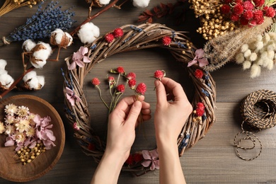 Photo of Florist making wreath with dried flowers at wooden table, top view