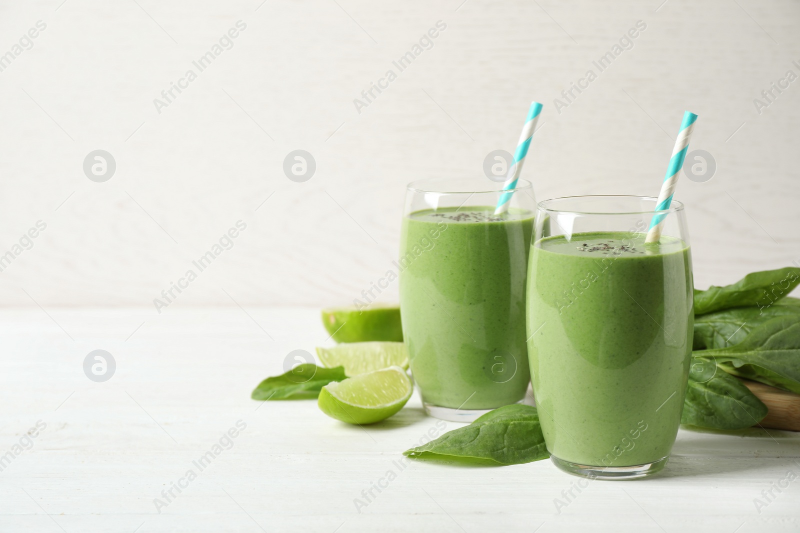 Photo of Glasses of healthy green smoothie with fresh spinach on white wooden table against light background. Space for text