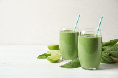 Photo of Glasses of healthy green smoothie with fresh spinach on white wooden table against light background. Space for text