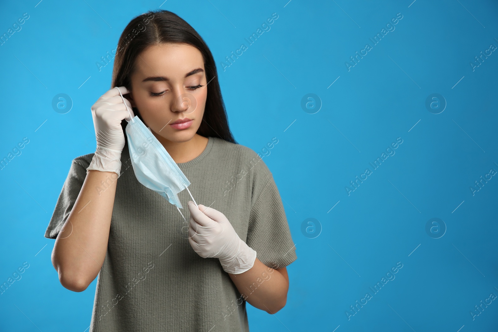 Photo of Woman in medical gloves putting on protective face mask against blue background. Space for text