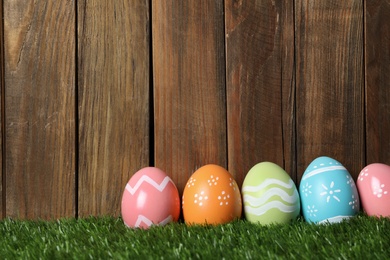 Photo of Colorful painted Easter eggs on green grass against wooden background, space for text