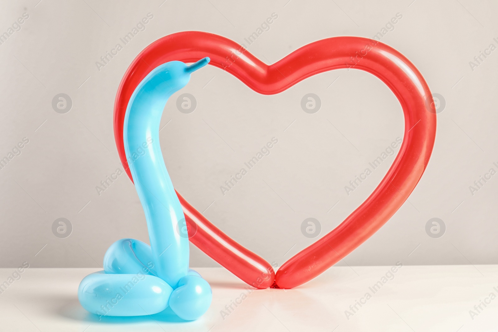 Photo of Snake and heart figures made of modelling balloons on table color light background