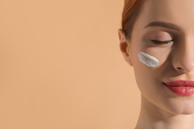 Beautiful young woman with sun protection cream on her face against beige background, closeup. Space for text