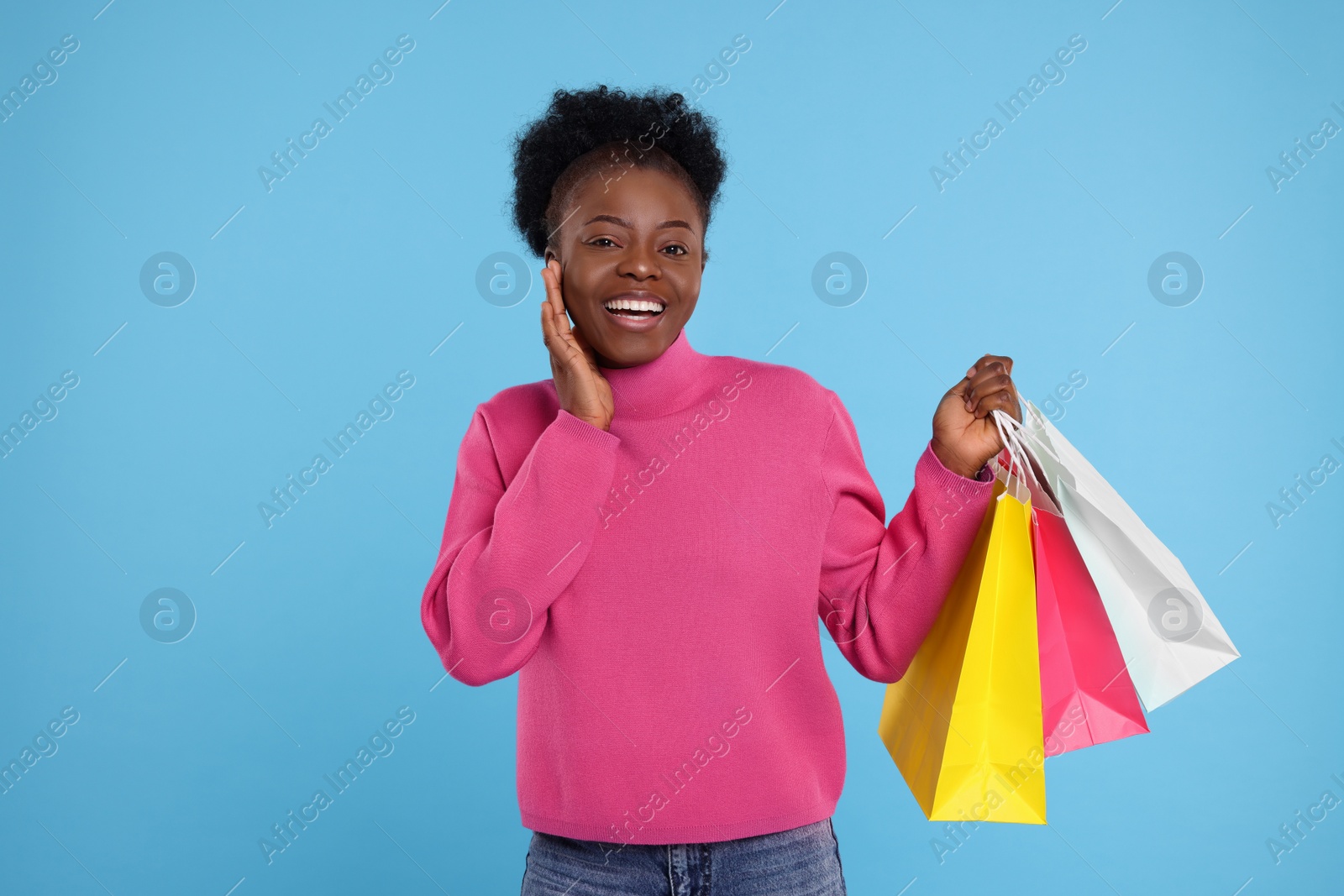 Photo of Happy young woman with shopping bags on light blue background