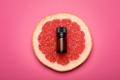 Photo of Bottle of citrus essential oil and fresh grapefruit slice on pink background, flat lay