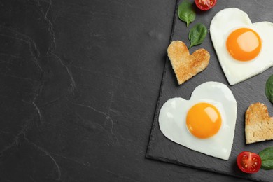 Photo of Heart shaped fried eggs and toasts on black table, top view. Space for text