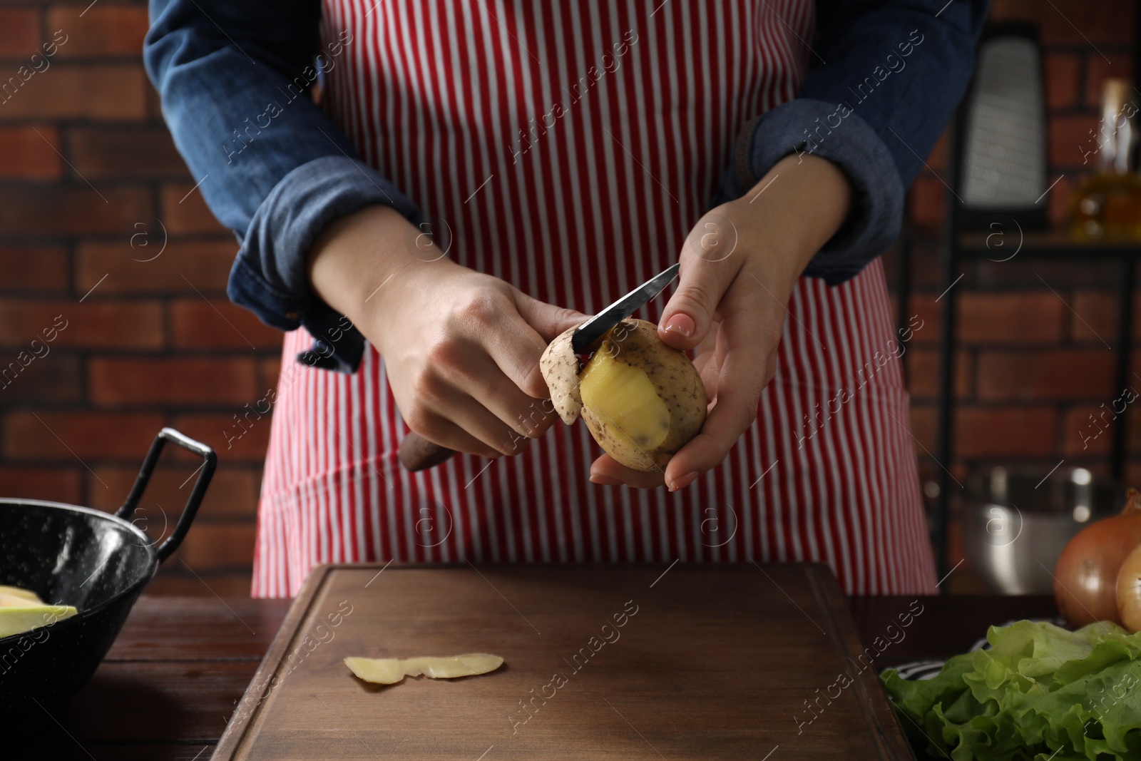Photo of Woman peeling fresh potato with knife at wooden table indoors, closeup