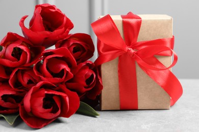 Beautiful gift box and bouquet of red tulip flowers on light table, closeup