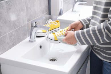 Woman washing stylish sneakers with brush in sink, closeup