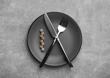 Photo of Plate with cutlery and word Anorexia made of wooden cubes on grey table, top view
