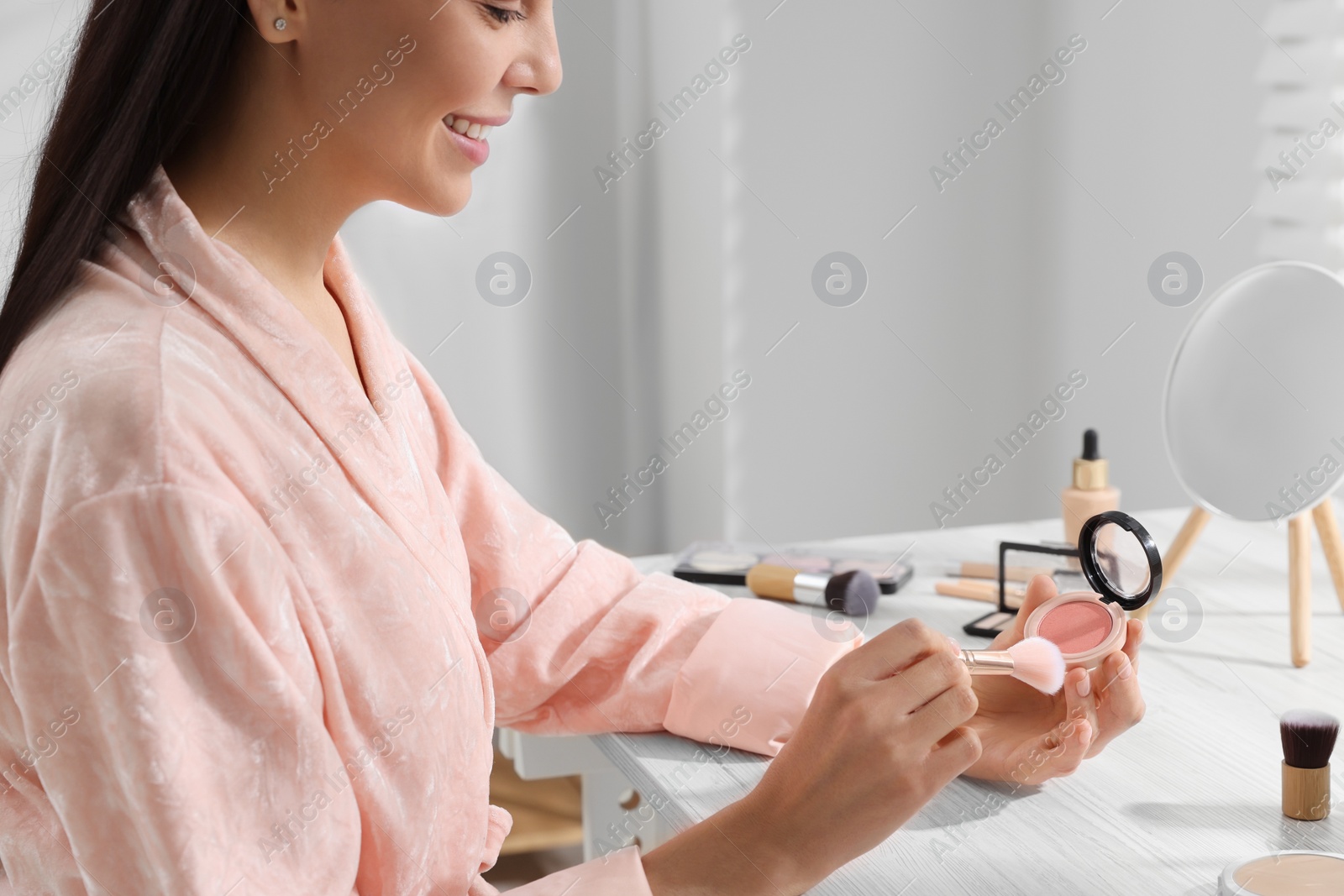 Photo of Woman with blusher and brush at dressing table indoors, closeup