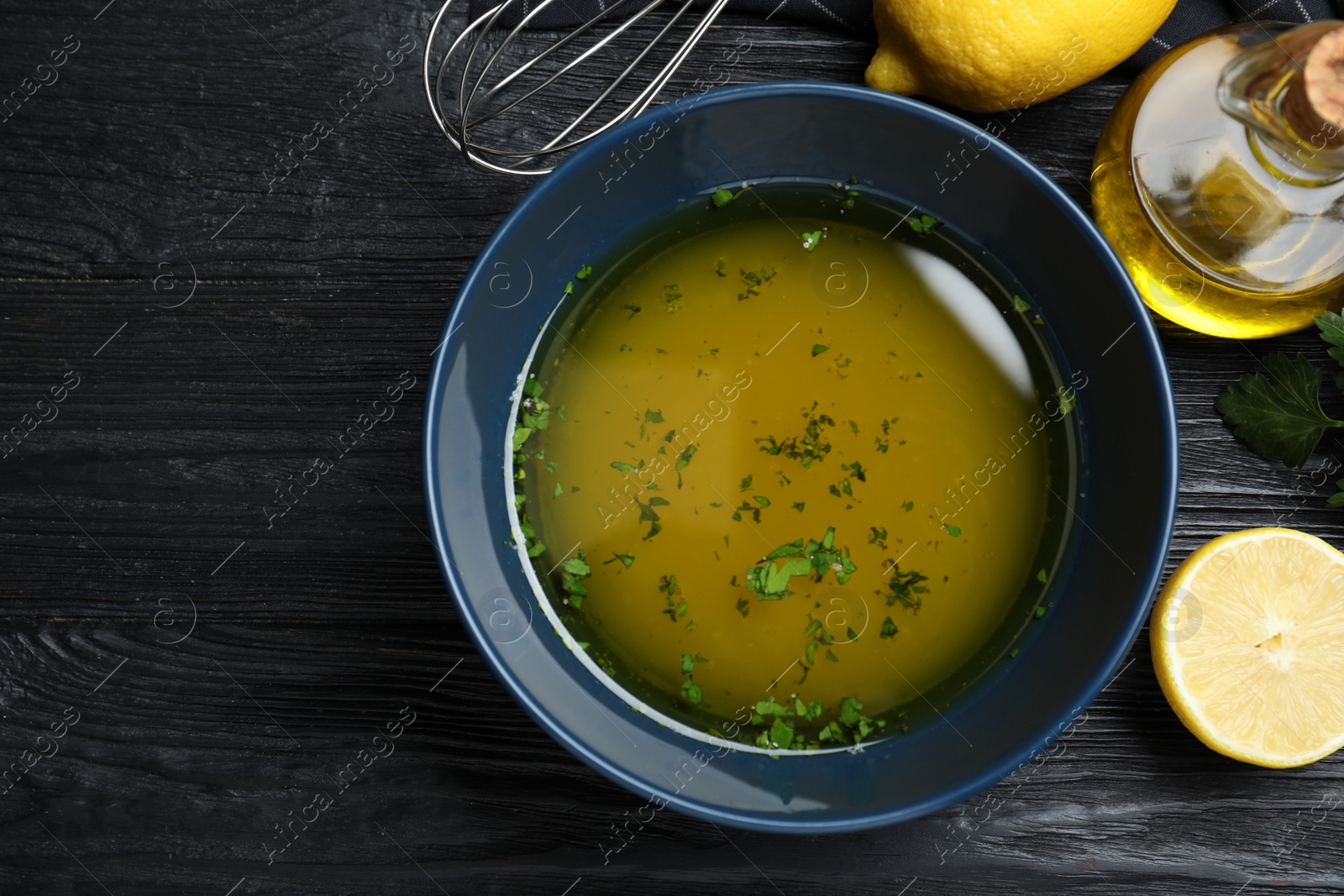 Photo of Bowl of lemon sauce and ingredients on black wooden table, flat lay. Delicious salad dressing