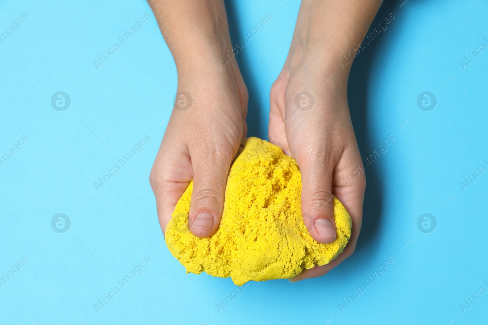 Photo of Woman playing with yellow kinetic sand on light blue background, top view