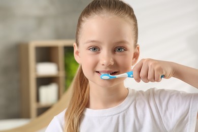 Photo of Cute little girl brushing her teeth with plastic toothbrush in bathroom, space for text