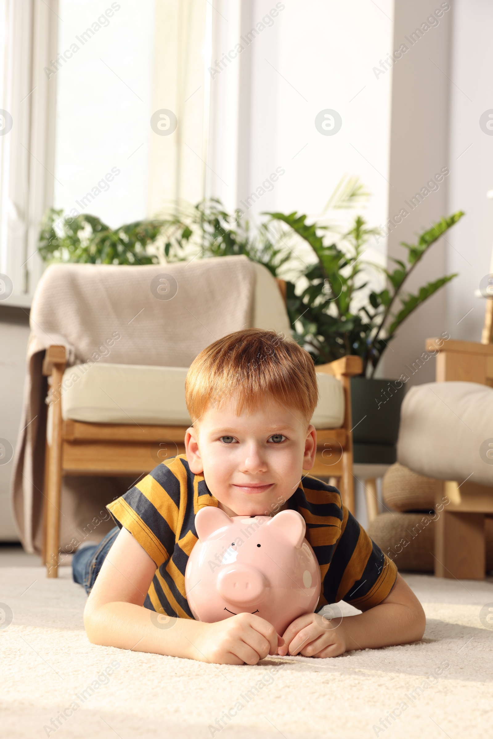 Photo of Cute little boy with ceramic piggy bank on floor at home