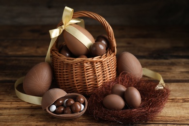 Composition with tasty chocolate eggs, wicker basket and decorative nest on wooden table