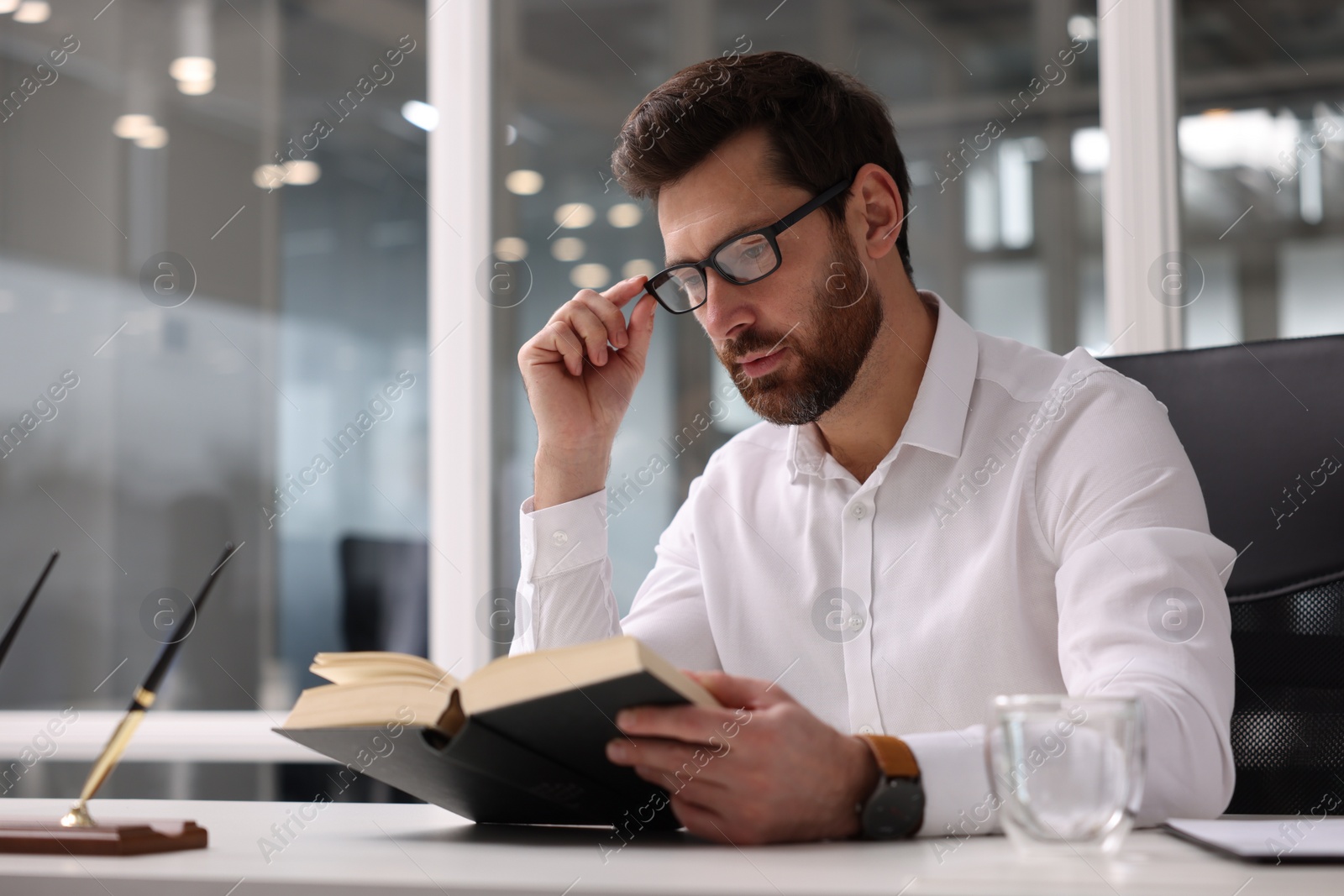 Photo of Handsome man reading book at table in office. Lawyer, businessman, accountant or manager