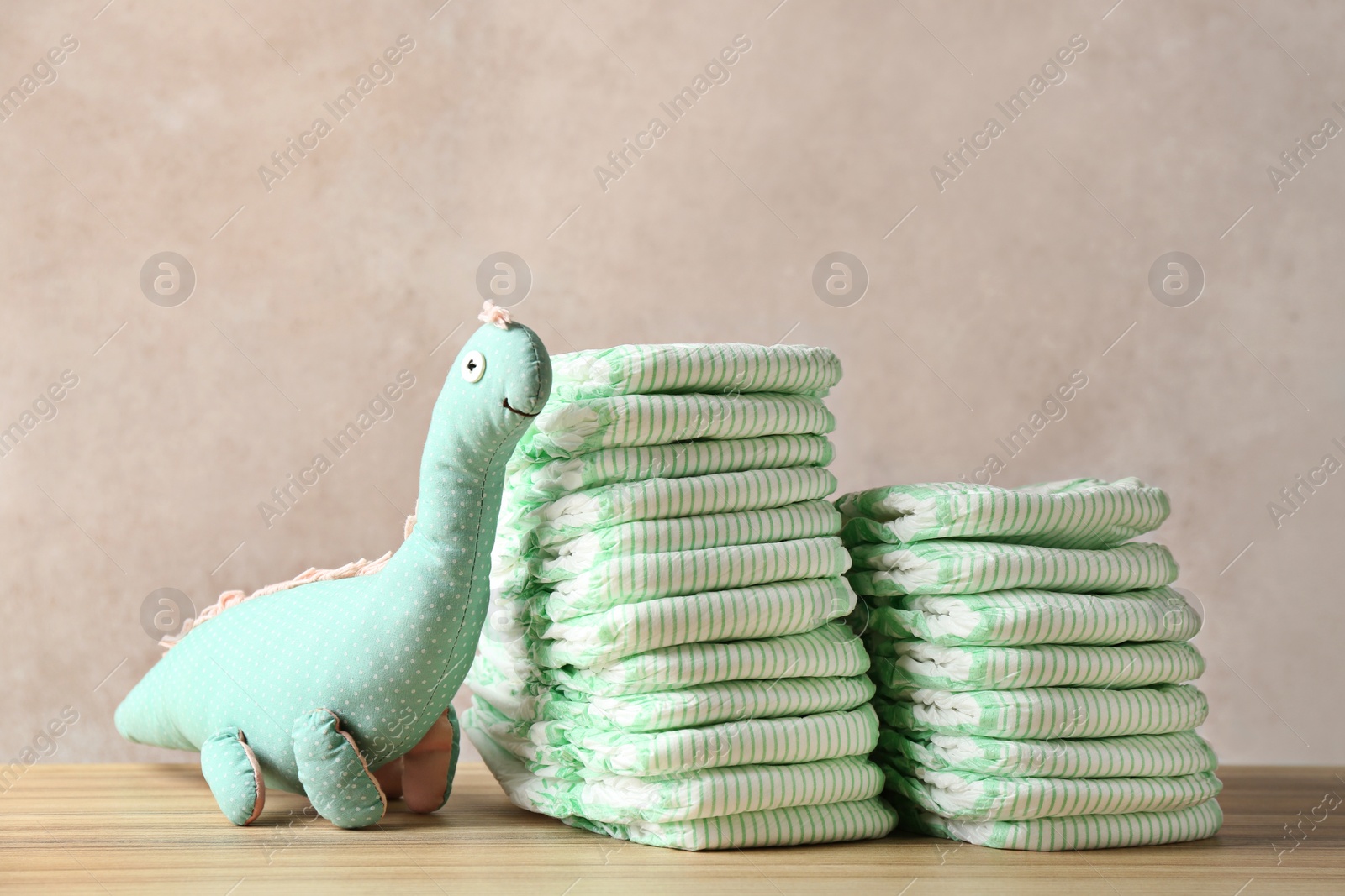 Photo of Stacks of diapers and toy dinosaur on table against color background. Baby accessories
