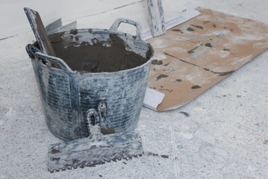 Photo of Bucket with cement and putty knifes indoors. Home improvement