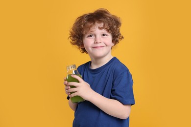 Photo of Cute little boy with glass bottle of fresh juice on orange background