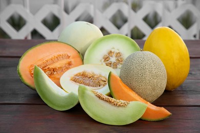 Different types of tasty ripe melons on wooden table outdoors