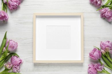Photo of Empty photo frame and beautiful flowers on white wooden table, flat lay. Space for design