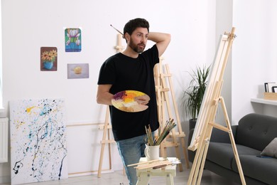 Photo of Man painting in studio. Using easel to hold canvas