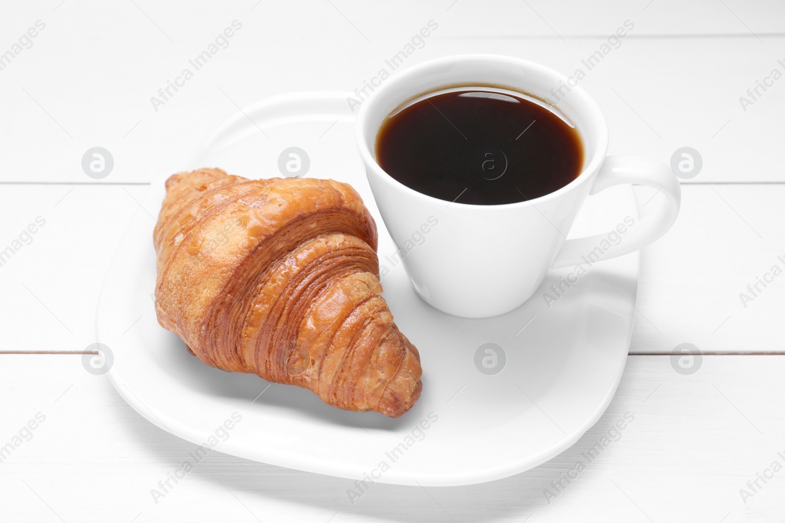 Photo of Tasty breakfast. Cup of coffee and croissant on white wooden table