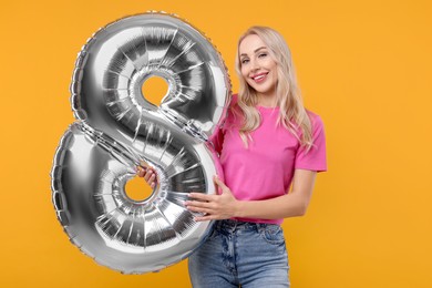 Photo of Happy Women's Day. Charming lady holding balloon in shape of number 8 on orange background