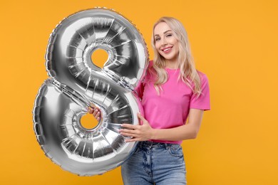 Happy Women's Day. Charming lady holding balloon in shape of number 8 on orange background