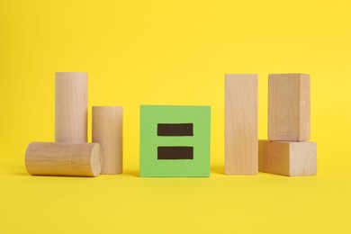 Wooden blocks and equals sign on yellow background