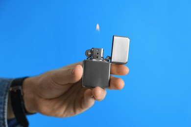 Photo of Man holding lighter with burning flame on light blue background, closeup. Space for text