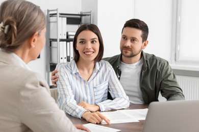 Young couple consulting insurance agent about pension plan at wooden table indoors