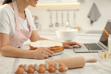Woman making cake while watching online cooking course via laptop in kitchen, closeup