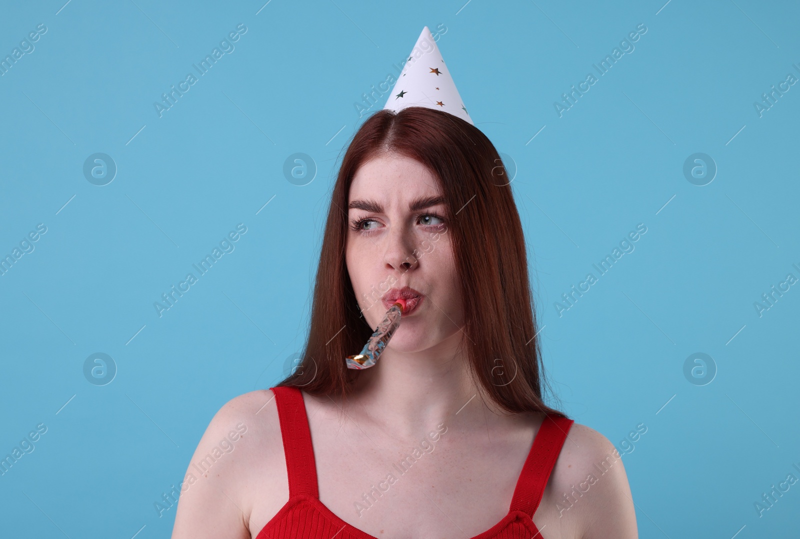 Photo of Sad woman in party hat with blower on light blue background