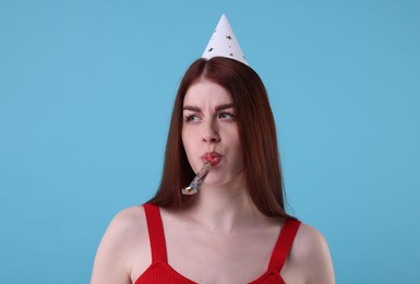 Photo of Sad woman in party hat with blower on light blue background
