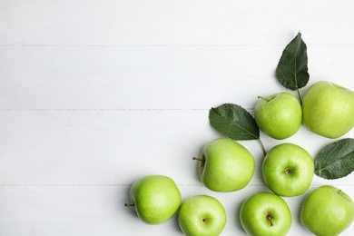 Photo of Ripe green apples and leaves on white wooden table, flat lay. Space for text