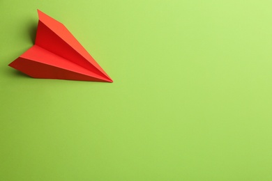 Red paper plane on green background, top view. Space for text