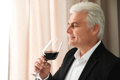 Senior man with glass of wine indoors. Space for text